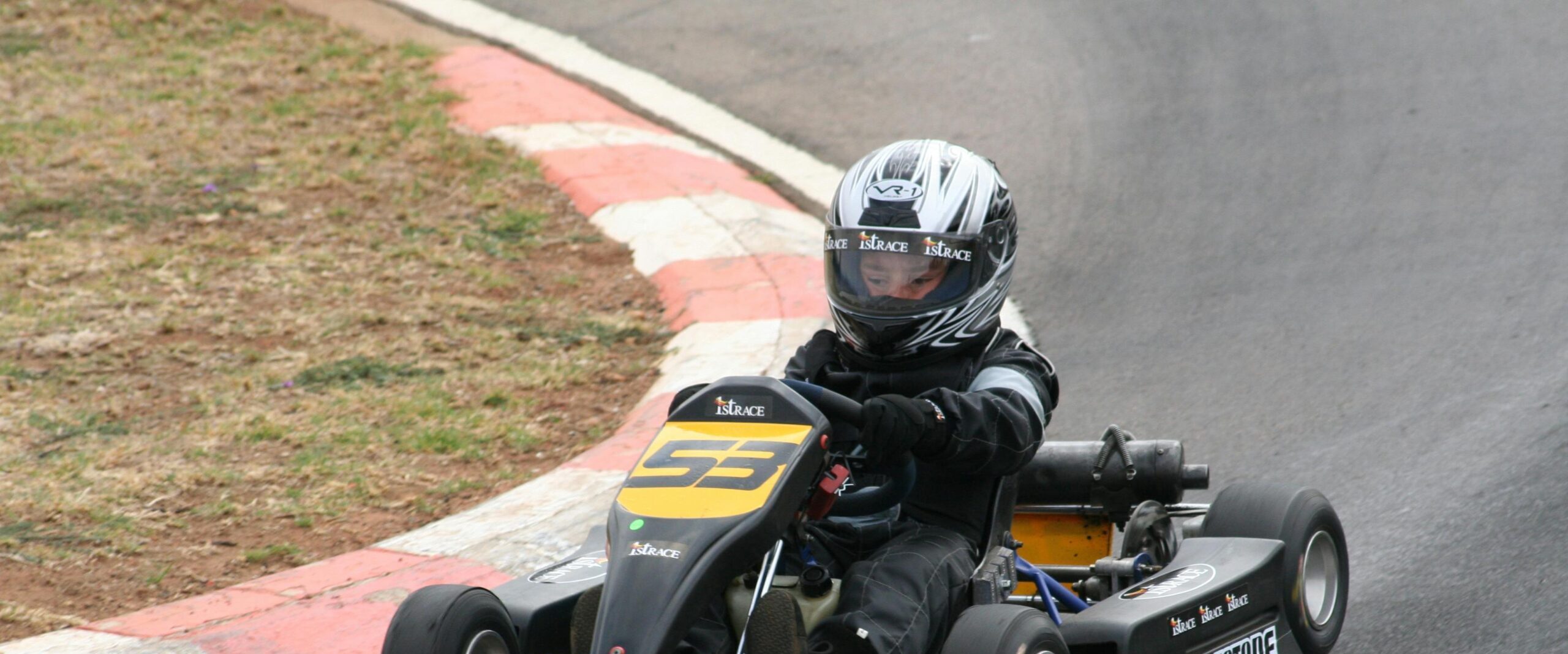 A young racer in full gear navigating a curve during a go-kart race on the track.
