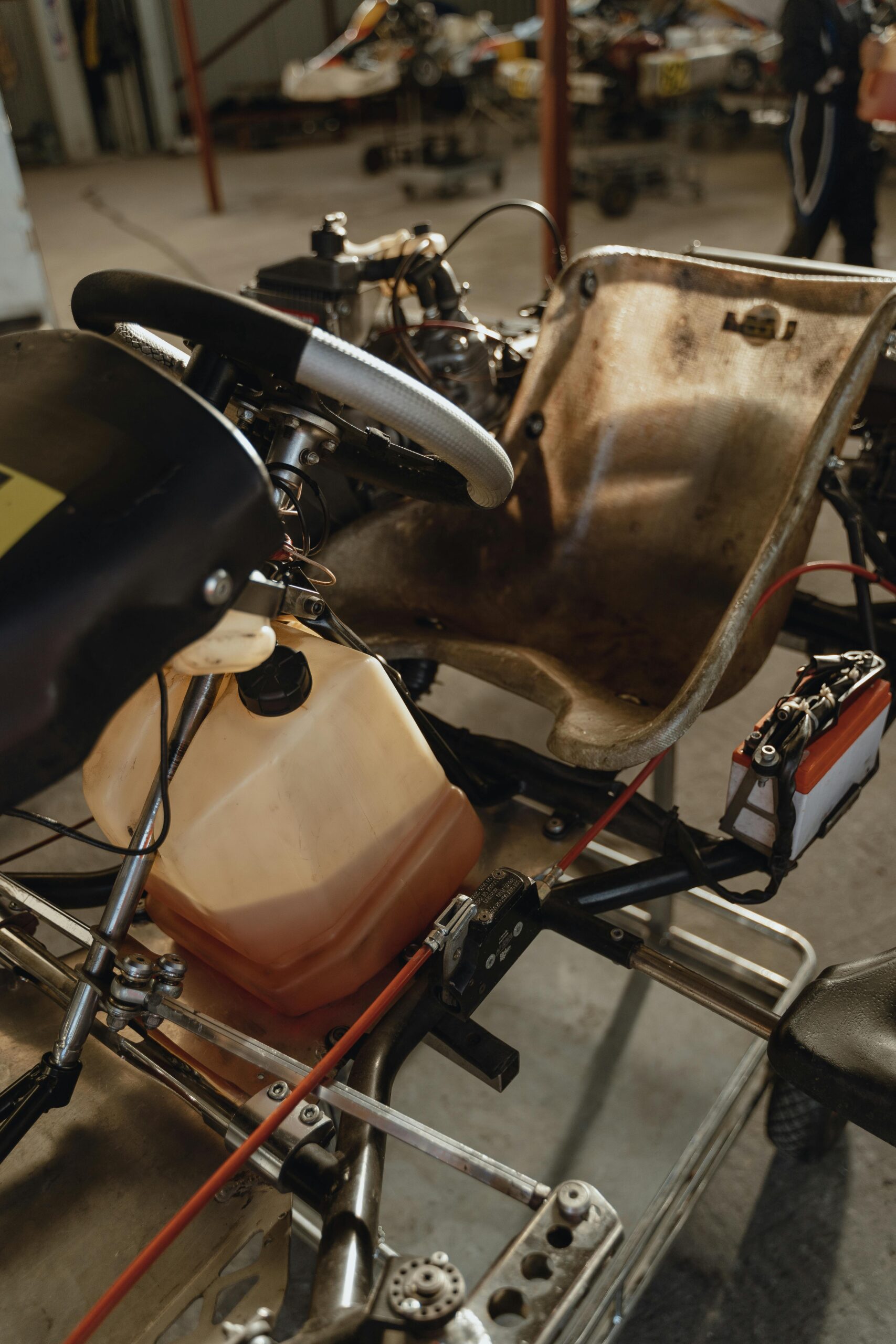 Detailed view of a go-kart chassis with steering wheel and fuel tank in a garage setting.